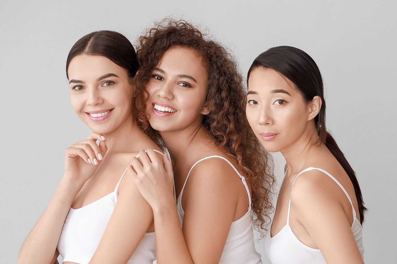Three women in white tops smiling against a neutral background.